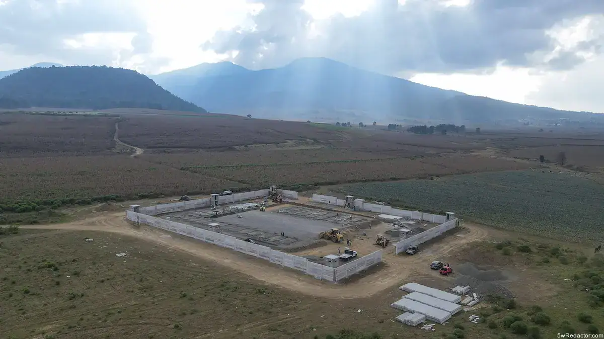 Muros de concreto en construcción en campo rural con montañas al fondo.