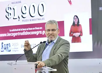 1. Hombre hablando en conferencia con pantalla de fondos de becas en segundo plano.