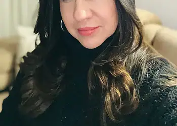 Rostro de mujer sonriendo, cabello largo y rizado, estilo natural, fondo de interiores, atractivo para contenido de belleza y estilo de vida.