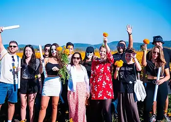 Niños en campo de flores con disfraces y flores en mano, celebración colorida y alegre en día soleado.