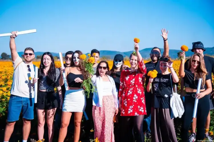 Niños en campo de flores con disfraces y flores en mano, celebración colorida y alegre en día soleado.
