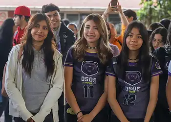 Chicas jóvenes en uniforme deportivo en evento escolar con otros estudiantes en el fondo.