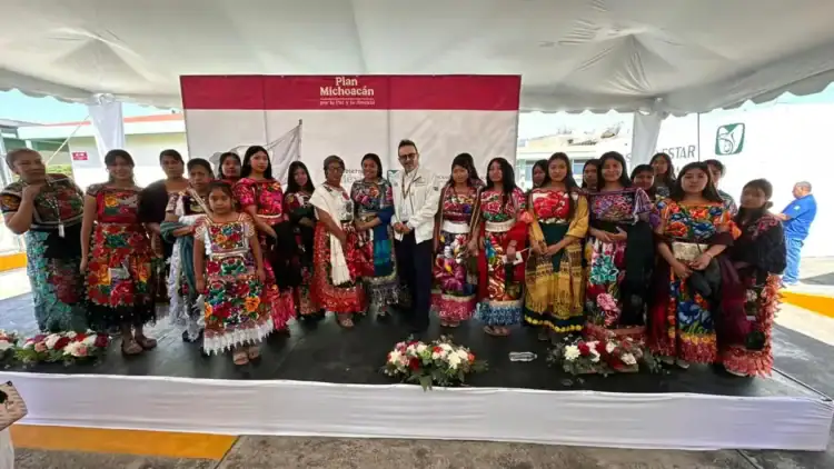 Vestido tradicional mexicano en un evento cultural con grupo de personas en un escenario.