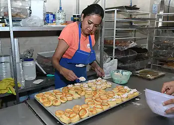 Mujer preparando y decorando pasteles en una cocina industrial.