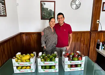 Pareja sonriendo con cajas de frutas en un establecimiento.