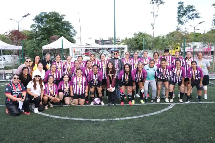 Equipo femenino de fútbol en uniforme morado y blanco en un campo de césped artificial.
